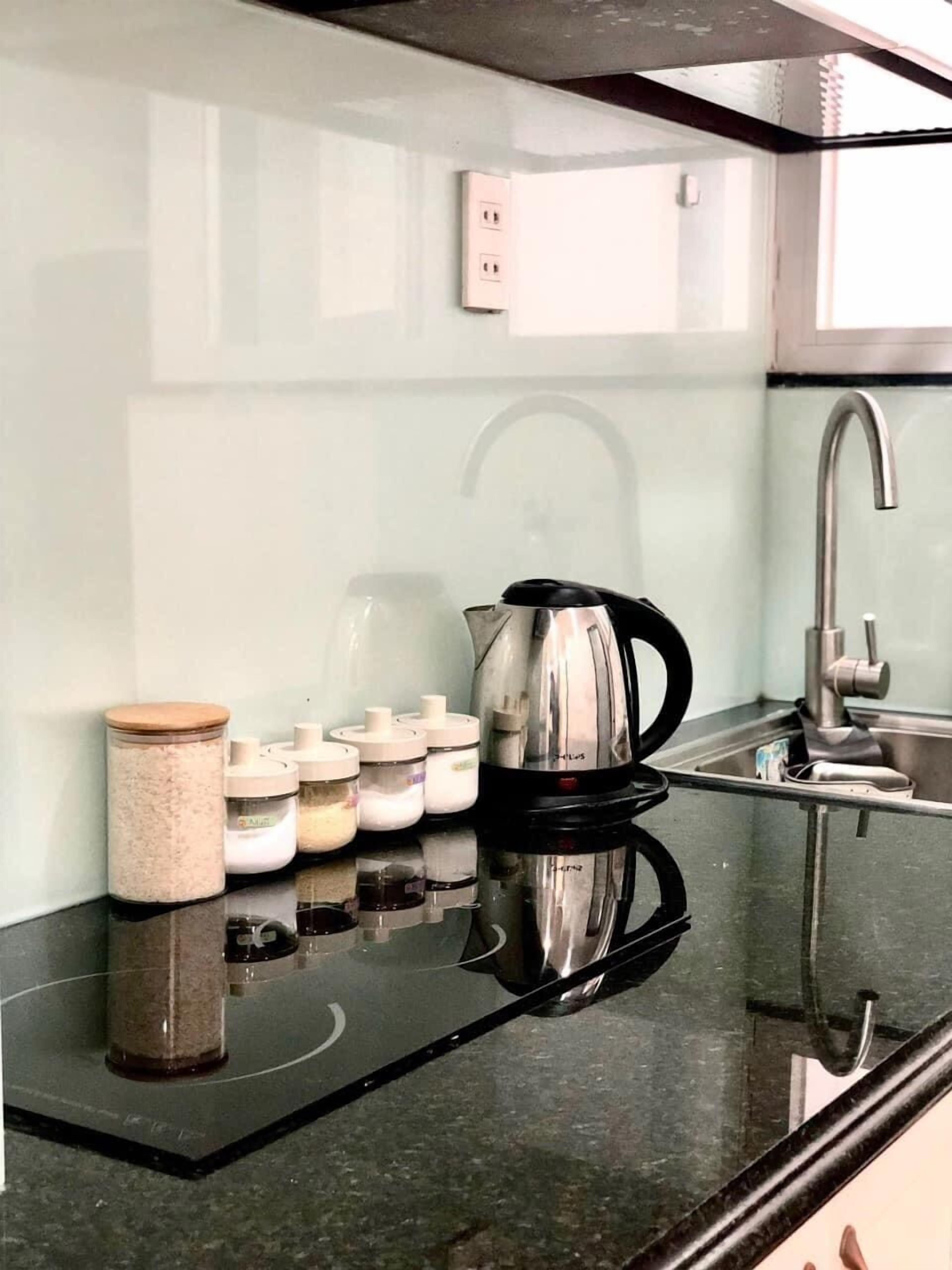 A kitchen with a black countertop, stainless steel kettle, and white storage jars.