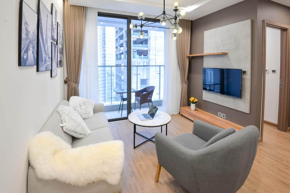 Ein modernes Wohnzimmer mit grauem Sofa, grauem Sessel, rundem Couchtisch und einem flachbildfernseher an der Wand.