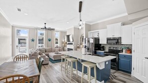 A modern kitchen with a central island, white cabinetry, and a dining area with a wooden table and chairs. - Steps from the Beach Pet Friendly HUGE Discounts for Sept!!!! (Panama City)