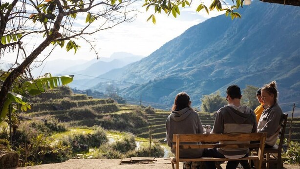 Three people sitting on a wooden bench overlooking terraced fields and mountains. - Hmong Sister House - Hostel (Ta Van)