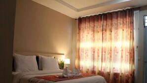 Une chambre d’hôtel avec un lit, une table de chevet, une lampe et une fenêtre ornée de rideaux à motifs floraux.