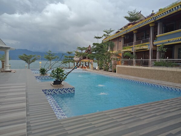 Una piscina con bordes de azulejos, un edificio con detalles en amarillo y vista al mar.