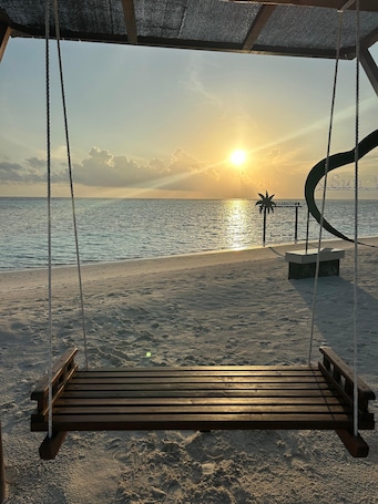 A wooden swing overlooking a beach with a sunset in the background.
