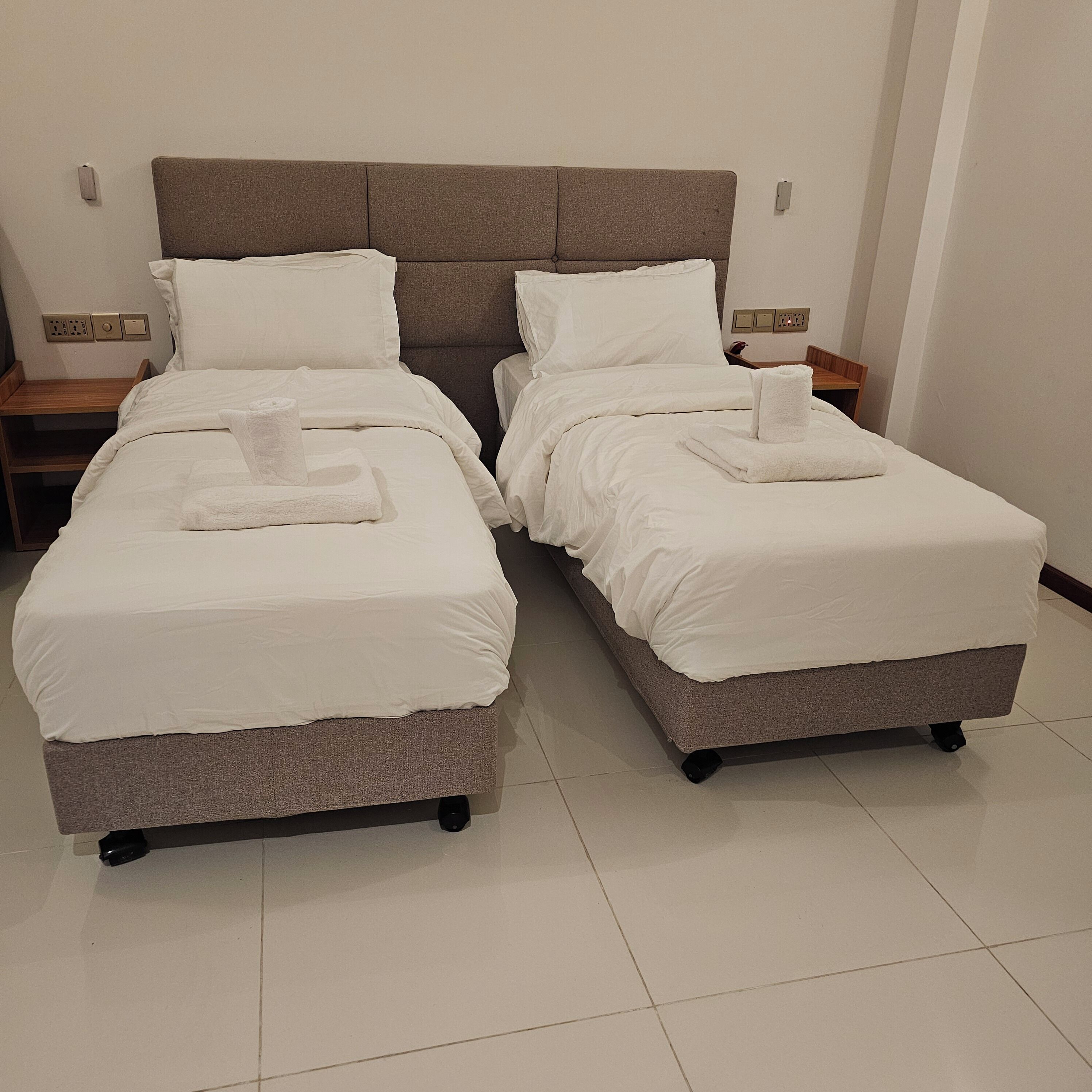A hotel room with two single beds, each with a white duvet and a folded towel.