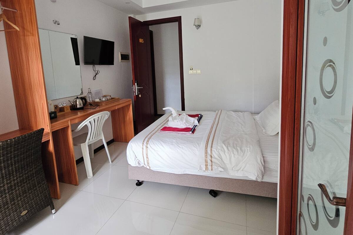 A hotel room with a bed, a desk, a chair, a television, and a ceiling fan.