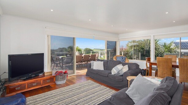 A spacious living room with a flat-screen TV, a grey sofa, wicker chairs, and a dining table. - Surf188 - sleeps up to 16 (SMITHS BEACH)