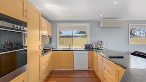 A modern kitchen with wooden cabinets, stainless steel appliances, a dishwasher, and a large window providing natural light. - Surf188 - sleeps up to 16 (SMITHS BEACH)