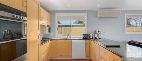 A modern kitchen with wooden cabinets, stainless steel appliances, a dishwasher, and a large window providing natural light.