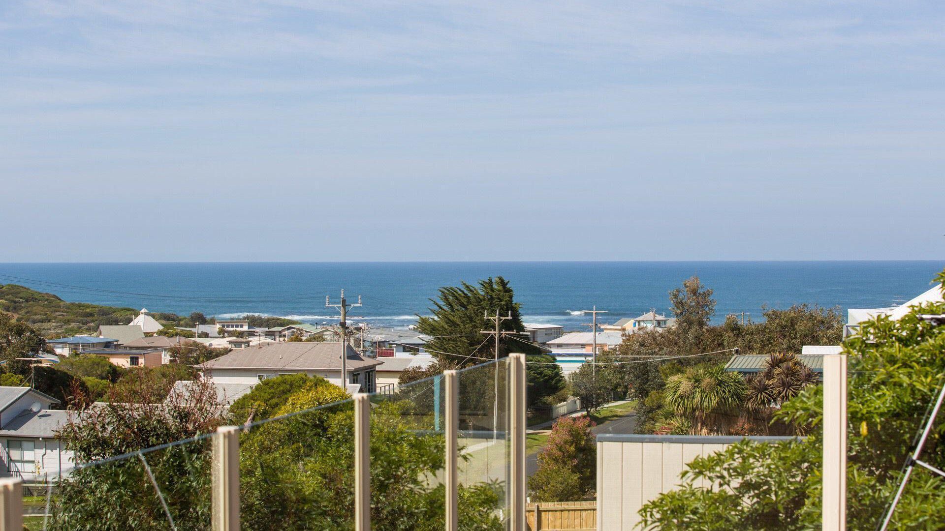 Un quartier résidentiel situé sur la côte, avec des maisons, une vue dégagée sur l’océan et une clôture au premier plan.