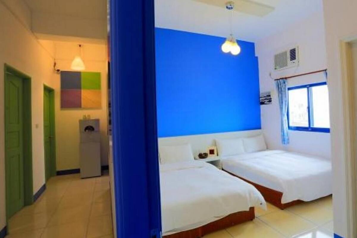 A hotel room with two beds, a blue accent wall, a ceiling fan, and a window with curtains.