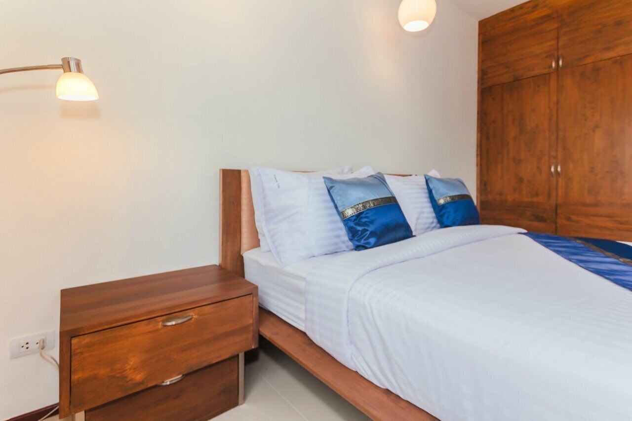 Een slaapkamer met een houten bed, wit beddengoed, een nachtkastje en een houten kledingkast.