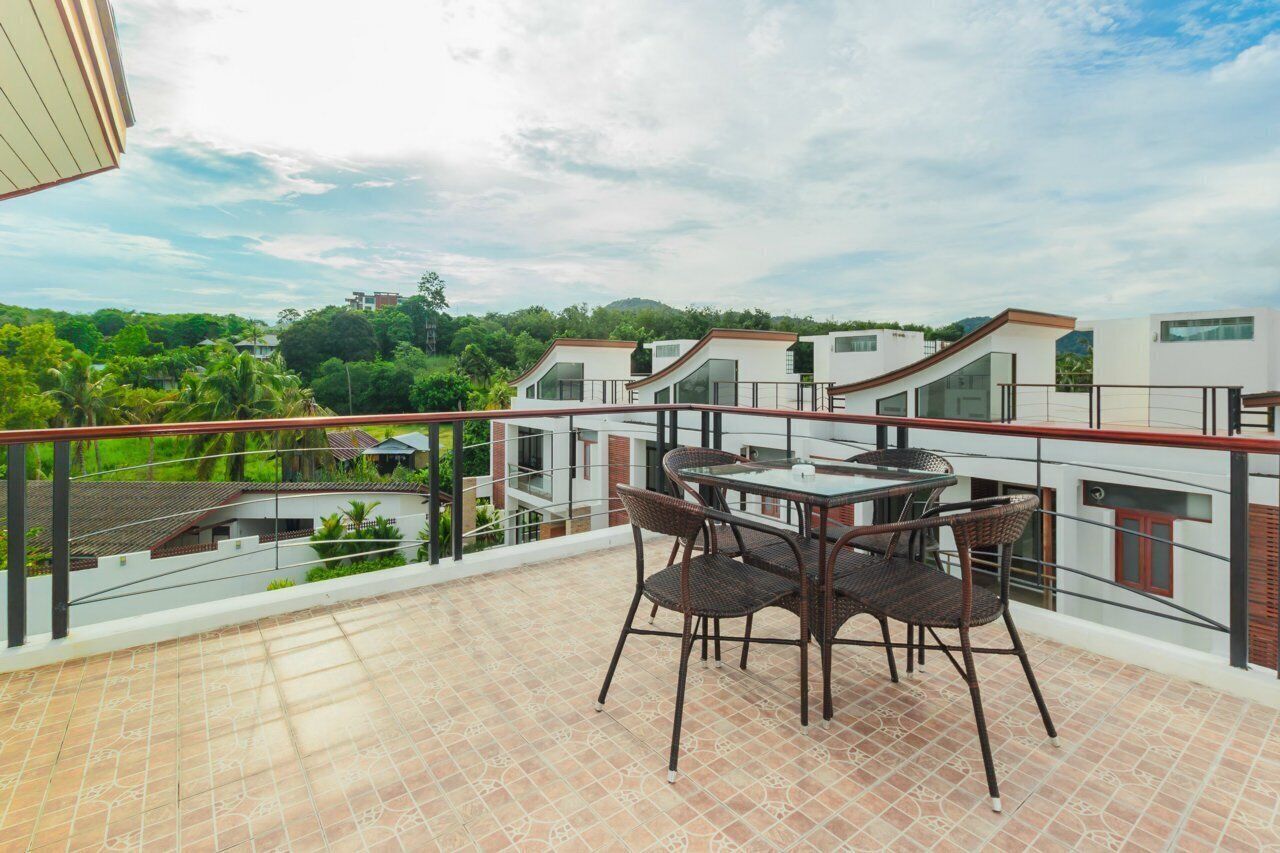 A balcony with a table and chairs, overlooking a residential area with modern houses and greenery.