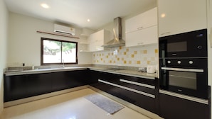 Cocina moderna con armarios negros, campana extractora de acero inoxidable, refrigerador negro y ventana con vista a follaje.