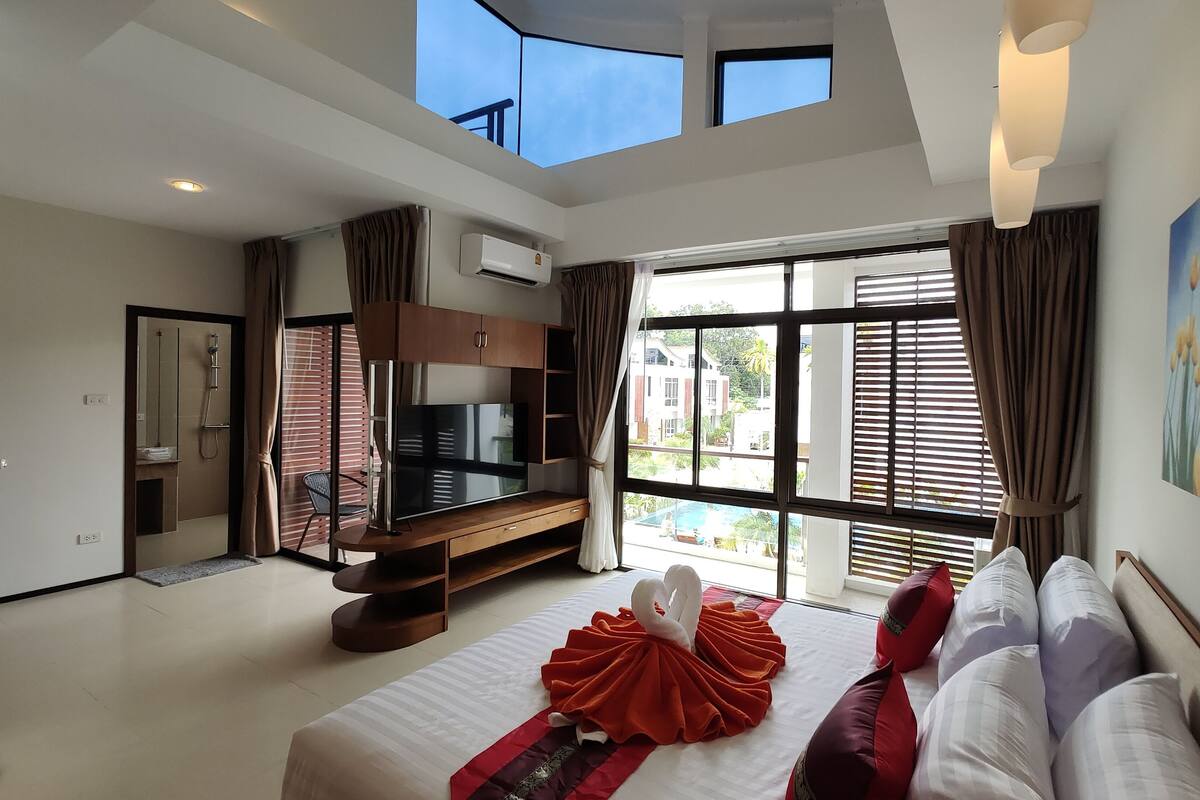 A modern hotel room with a large bed, a TV, and a balcony with a pool view.