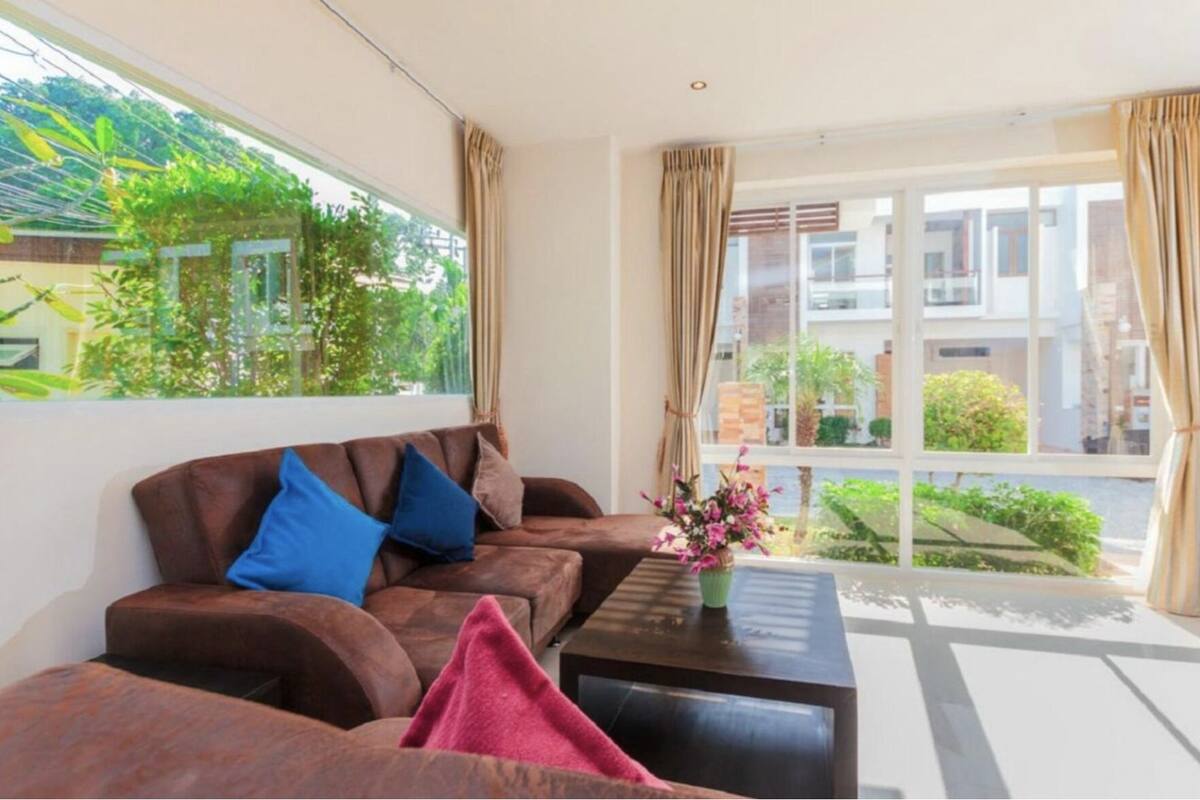 A modern living room with a brown sofa set, a coffee table, and a view of greenery outside.