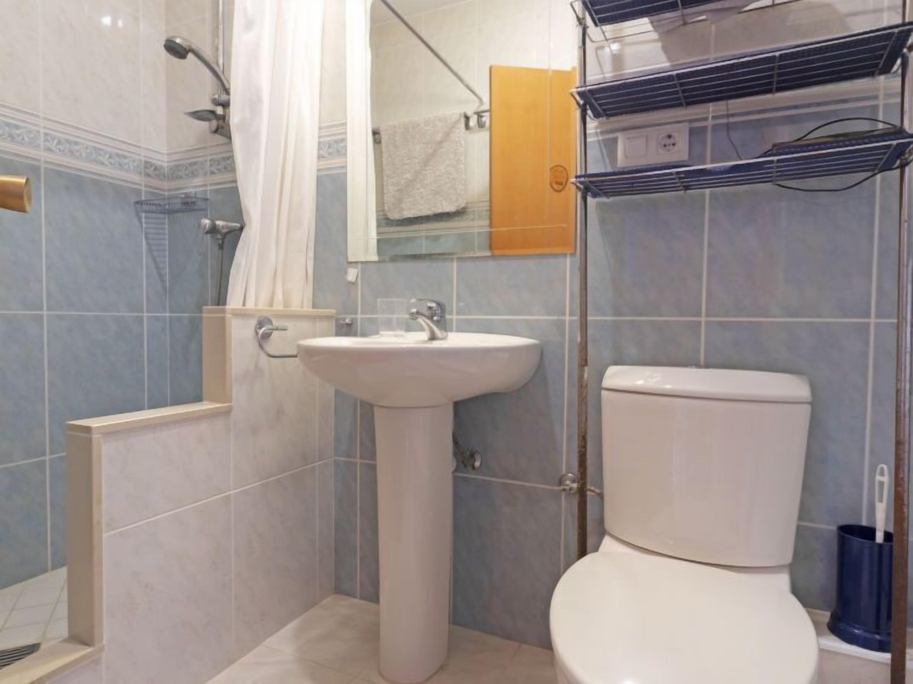 A bathroom with a pedestal sink, a toilet, a shower with a curtain, and a towel rack.
