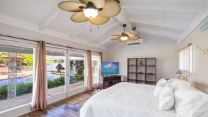 Une chambre dotée d’un grand lit, d’une télévision, d’un ventilateur de plafond et offrant une vue sur une piscine.