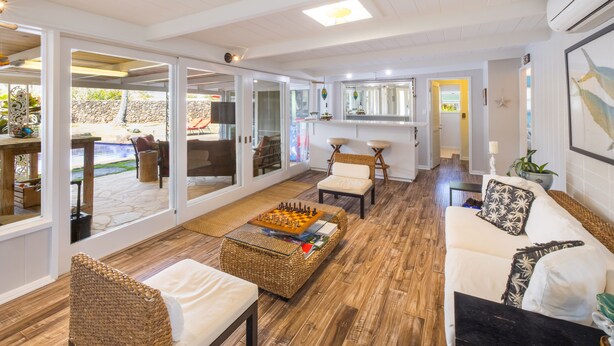 Un vaste espace de vie doté d’un plancher en bois, de canapés blancs, d’une table d’échecs et d’une grande porte vitrée donnant sur un patio extérieur.