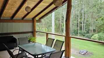 An outdoor patio with a glass table and chairs, surrounded by wooden beams and a view of the forest.