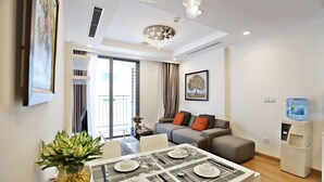A modern living room with a dining area, a water dispenser, and a large window. - Bom Homestay Vinhomes Times City (Hanoi)