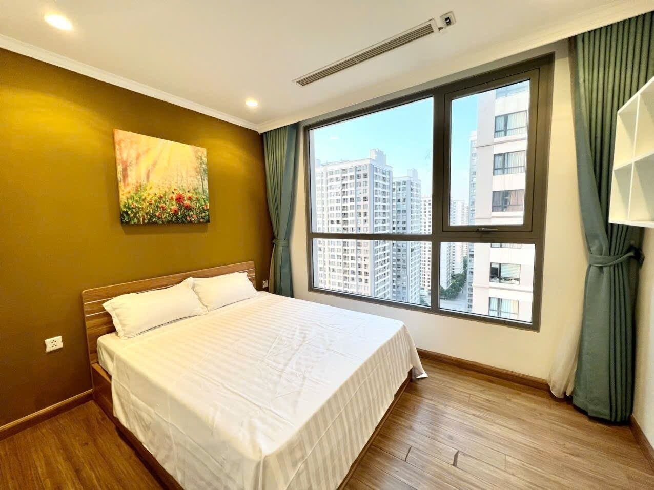 Ein Hotelzimmer mit einem großen Bett, einem Fenster mit Blick auf die Stadt und einem Gemälde an der Wand.