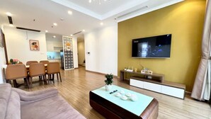 A modern living room with a sofa, coffee table, TV, and dining area. - Bom Homestay Vinhomes Times City (Hanoi)