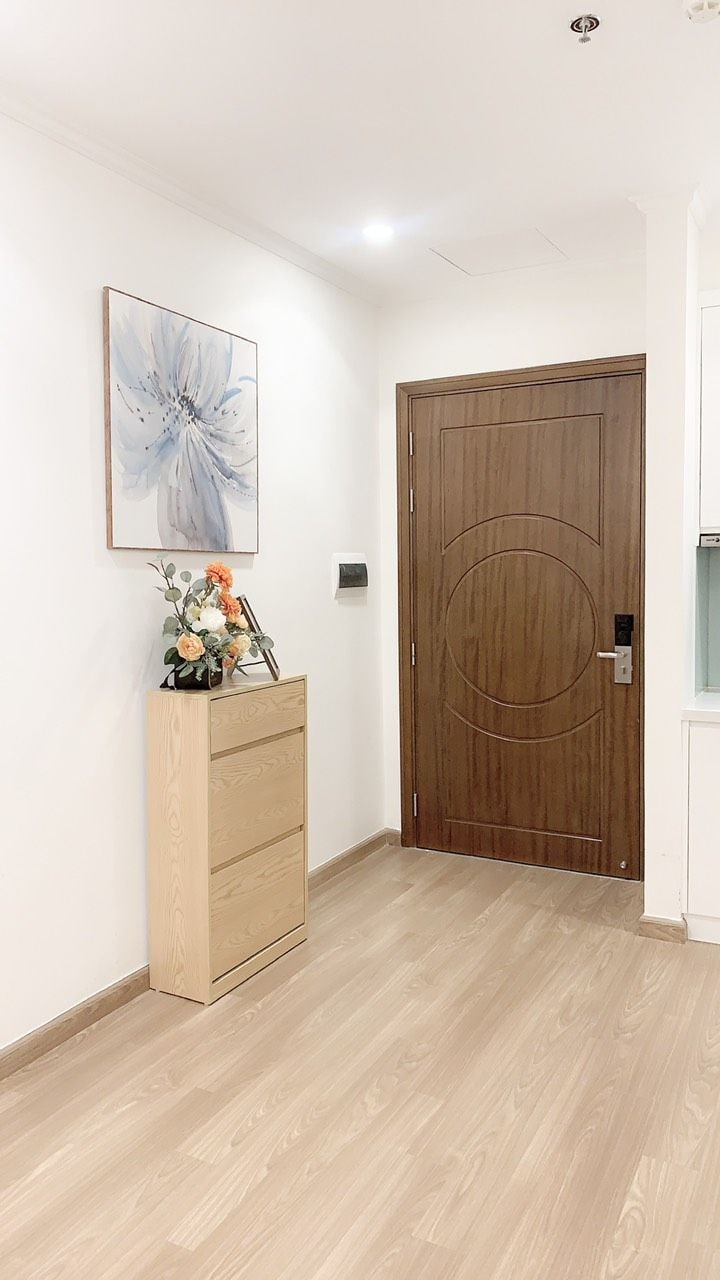 A hallway with a wooden door, a wooden cabinet with drawers, and a framed floral artwork on the wall.