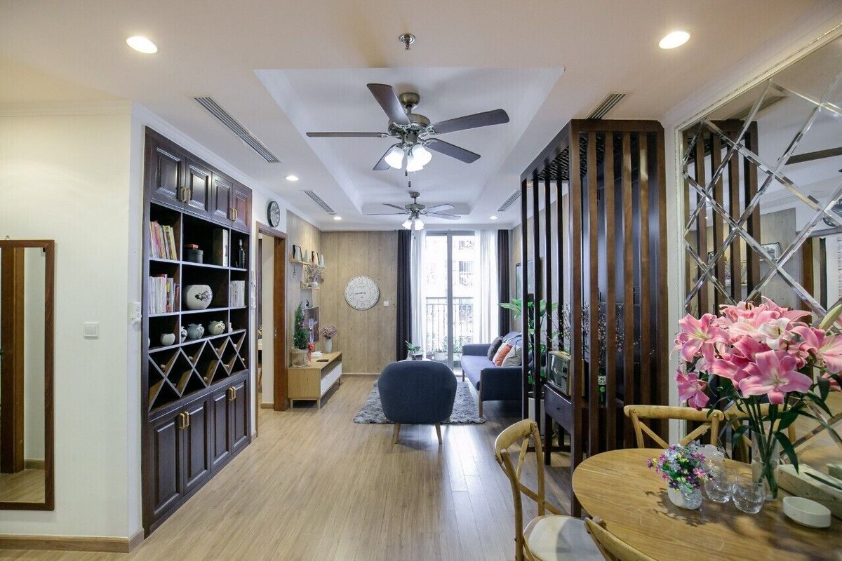 A modern living room with a ceiling fan, built-in bookshelves, a wooden dining table, and a large window.