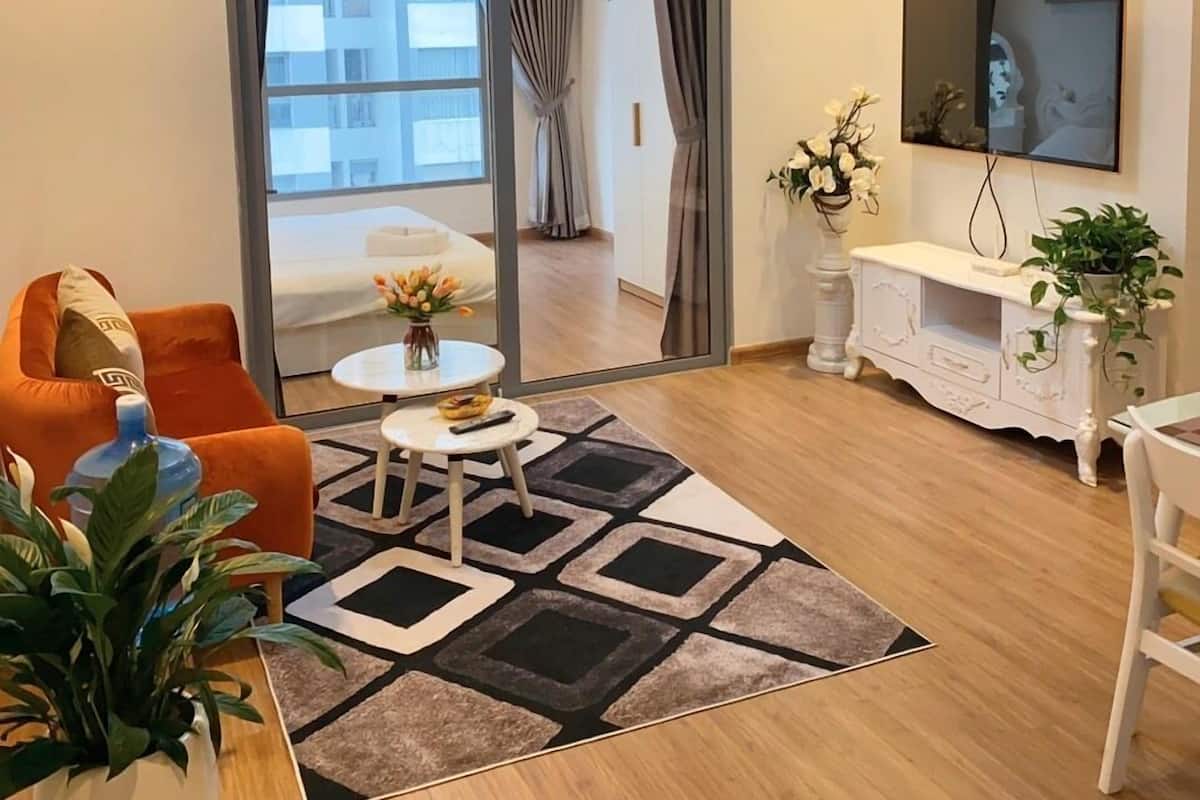 A modern living room with a sofa, coffee table, and TV. There is a large window with curtains, a plant, and a white cabinet.