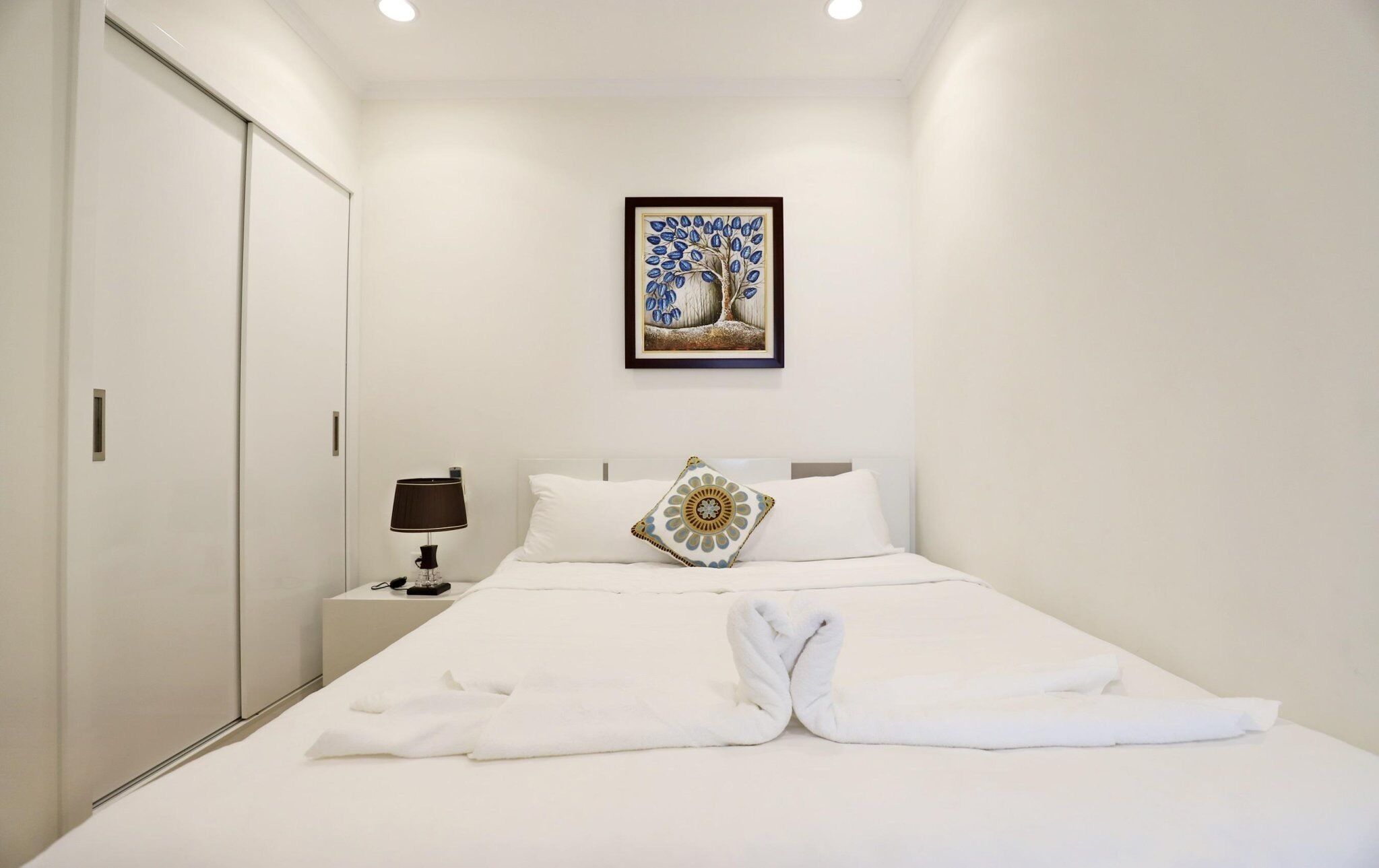 Une chambre d’hôtel avec un lit bien fait, une lampe de chevet, une œuvre d’art encadrée au mur et une armoire.