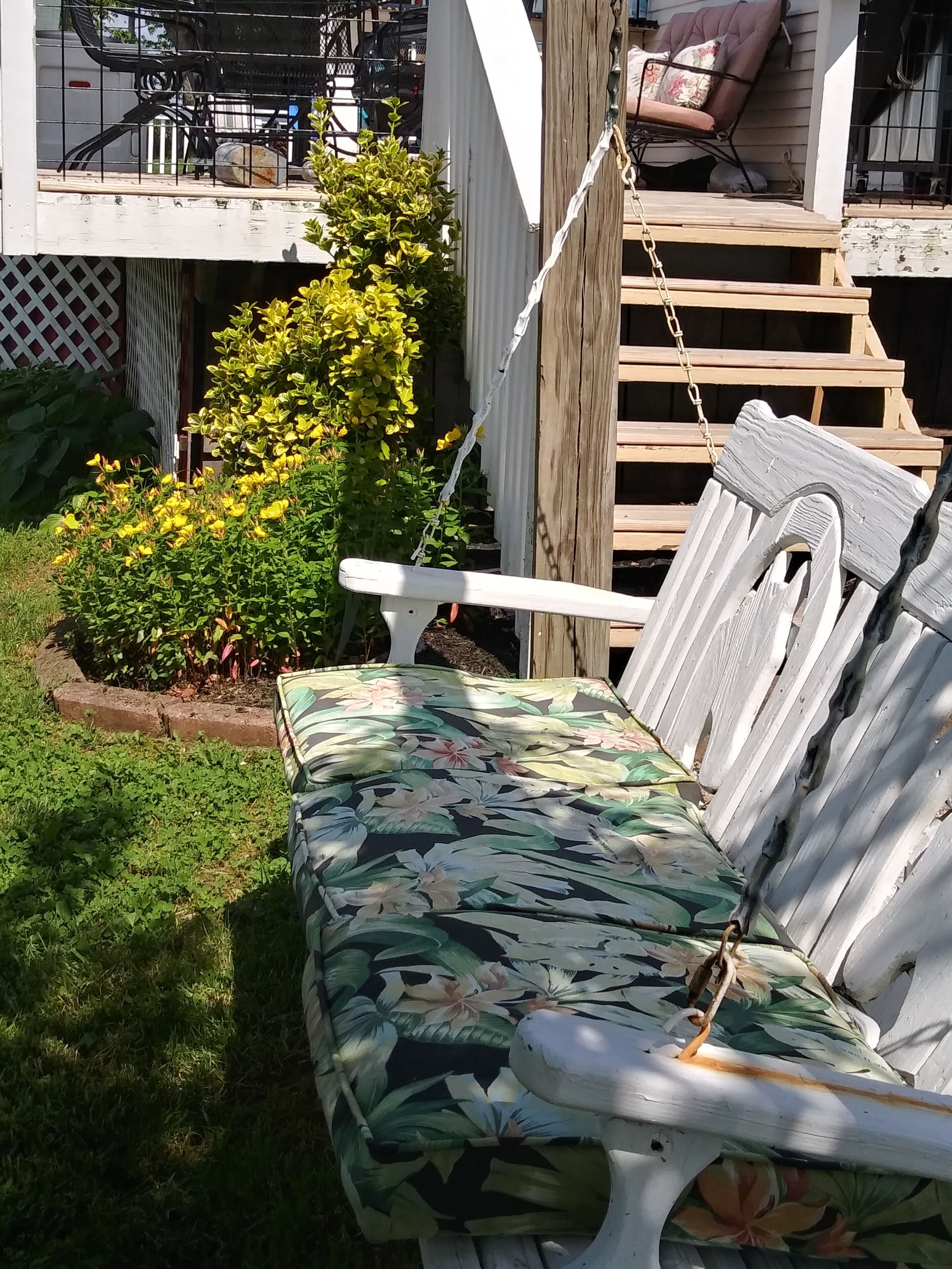 A wooden deck with a white bench and a small garden area with yellow flowers and green foliage.