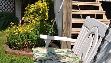 A wooden deck with a white bench and a small garden area with yellow flowers and green foliage.