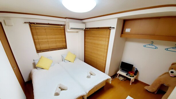 A small, well-lit room with a bed, a desk, a chair, a teddy bear, and a television. - Hosei Apartment 201 (Kobe)
