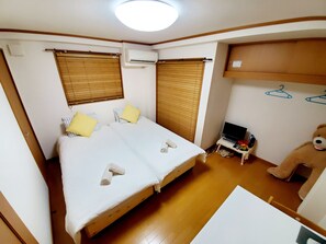 A small, well-lit room with a bed, a desk, a chair, a teddy bear, and a television. - Hosei Apartment 201 (Kobe)