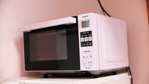 A white microwave on a white appliance, with a control panel displaying various settings and a power button. - Hosei Apartment 201 (Kobe)