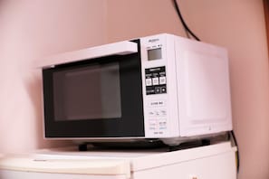 A white microwave on a white appliance, with a control panel displaying various settings and a power button. - Hosei Apartment 201 (Kobe)