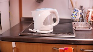 A kitchen with a white kettle on a induction cooktop, a kettle cord, and a tray with utensils. - Hosei Apartment 201 (Kobe)