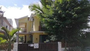 Ein zweistöckiges Haus mit Balkon, umgeben von üppigem Grün und einem befestigten Eingang.