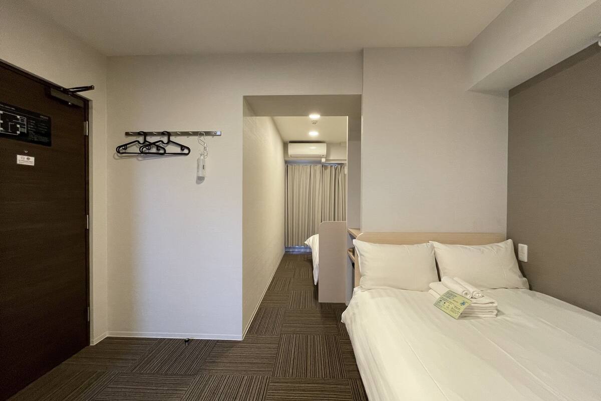 Ein Hotelzimmer mit Bett, Kleiderständer, einer Tür und einem Flur, der zu einem Badezimmer führt.