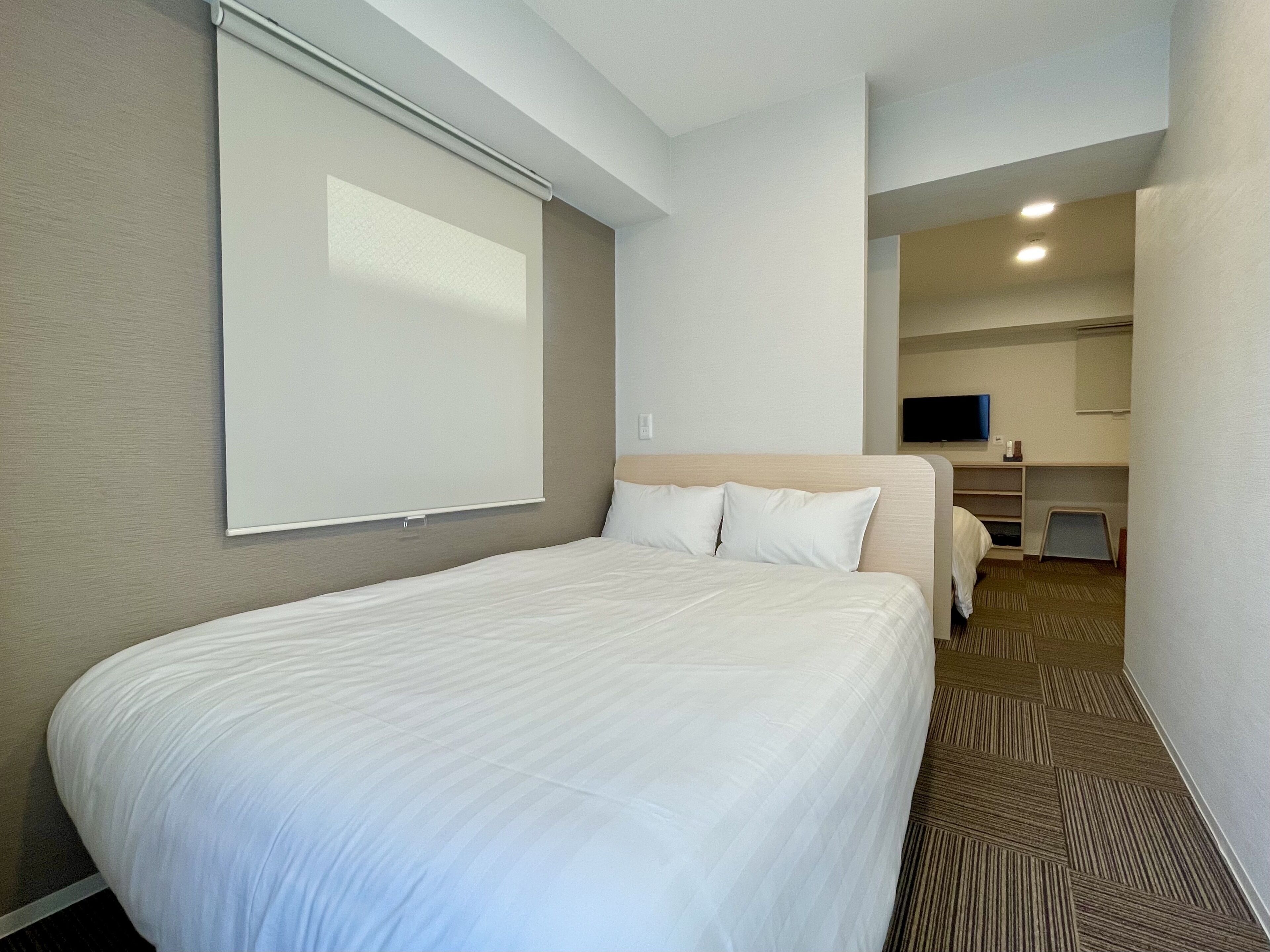 A hotel room with a large bed, a flat-screen TV mounted on the wall, and a small desk with a chair.