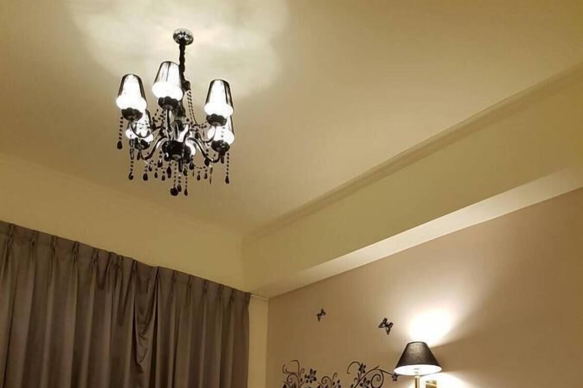 A hotel room with two beds, a chandelier, a wall-mounted lamp, and a decorative wall piece.