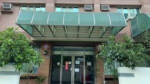 Un edificio de varios pisos con un toldo verde sobre la entrada. Hay unidades de aire acondicionado en la fachada, y la entrada tiene puertas de vidrio con un felpudo rojo.