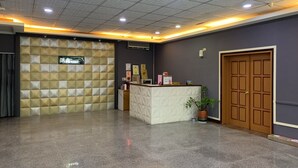 Zona de recepción con mostrador de check-in, una pared decorativa, una planta en maceta y una puerta de madera.