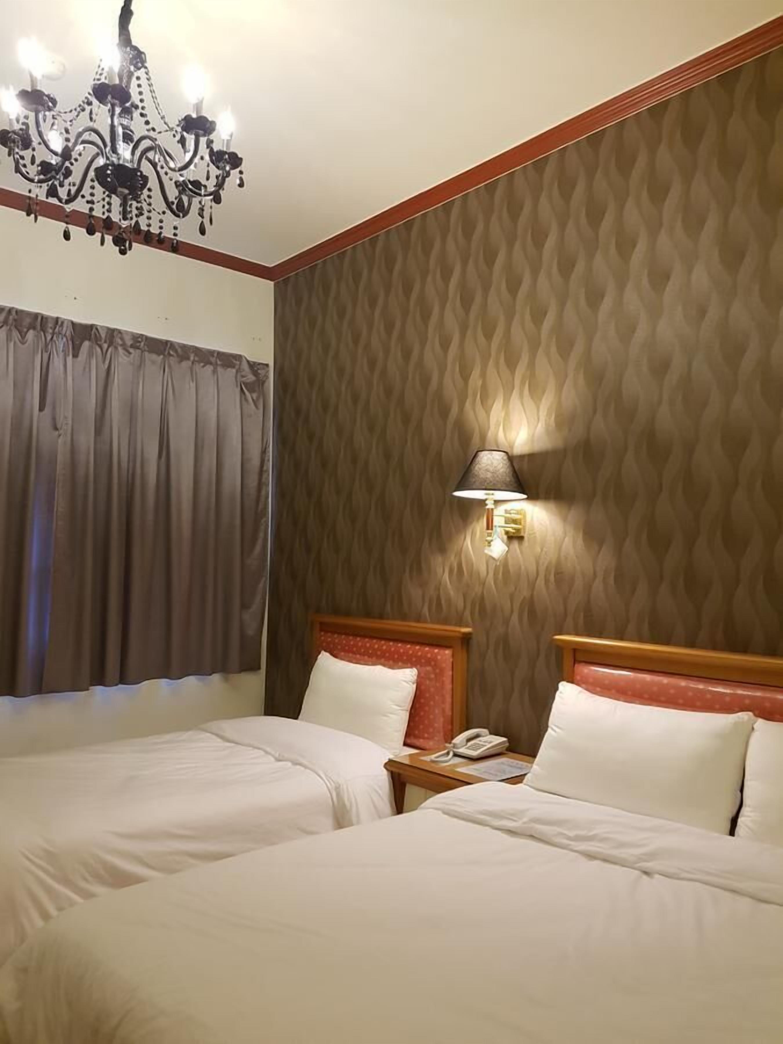 Een hotelkamer met twee bedden, een kroonluchter, een lamp en een behang met patroon.