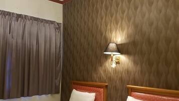 Een hotelkamer met twee bedden, een kroonluchter, een lamp en een behang met patroon.