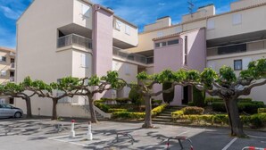 Un edificio residencial de varios pisos con balcones y un estacionamiento con árboles y pilares.