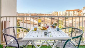 Un balcón con una mesa blanca dispuesta para el desayuno, dos sillas y vistas a edificios.