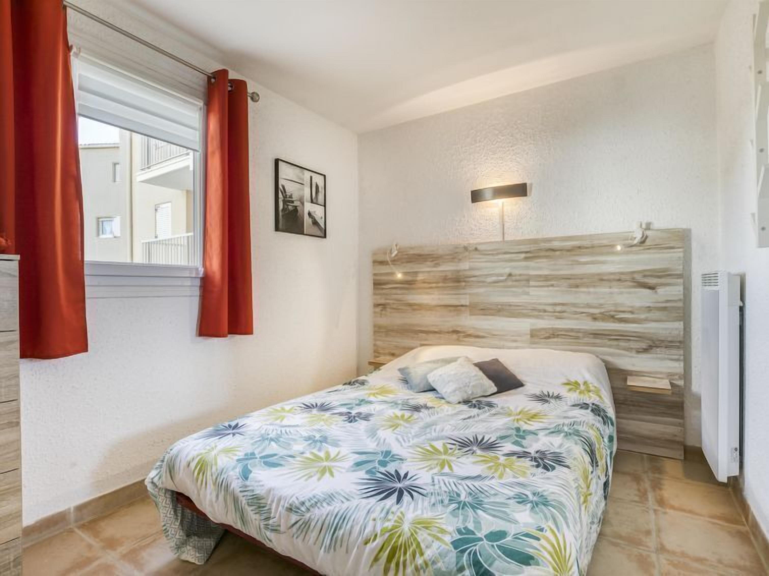 A bedroom with a bed, a headboard, a window with curtains, and a wall-mounted light.