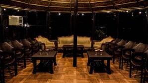 Un espace intérieur à l’éclairage tamisé, doté d’un plancher en bois, de chaises rembourrées et de tables disposées pour les repas ou les moments de convivialité.