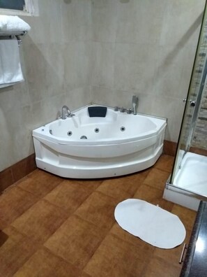 A bathroom with a freestanding bathtub, a shower area, and a white bath mat on the floor. - Jungle Leela Resort (Ramnagar)